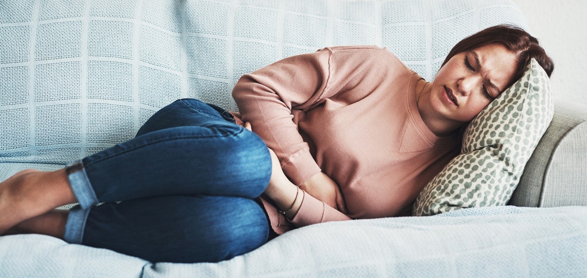 a woman lying on couch holding her stomach showing stomach pain