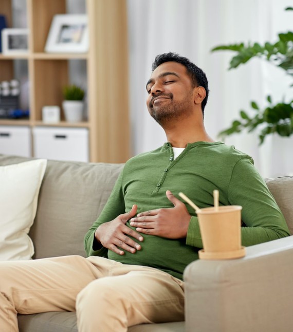 a man sitting in couch gesturing his stomach is full